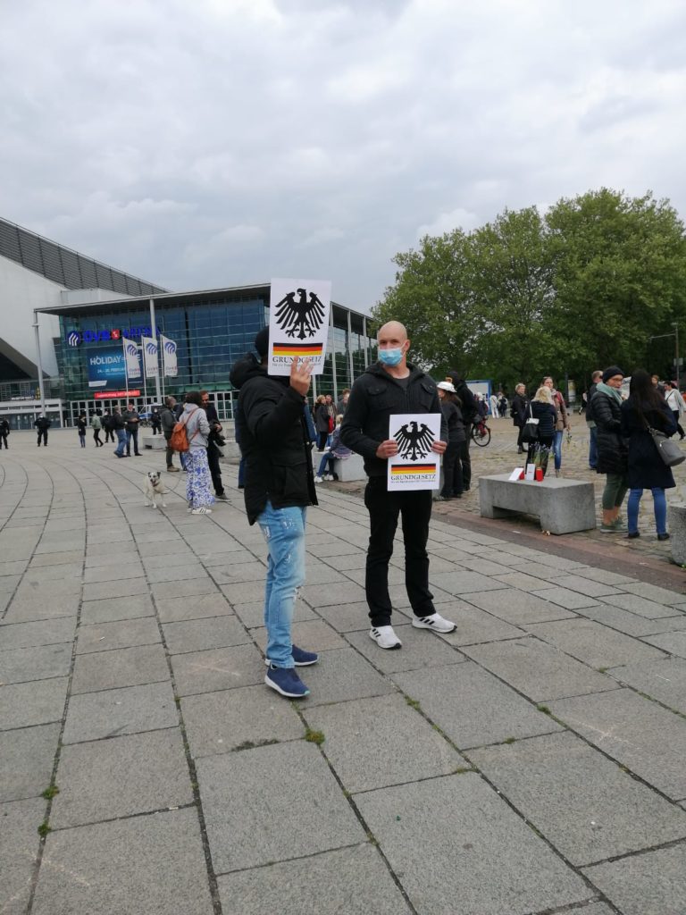 Zwei Männer auf der Demonstration, sie halten je ein Blatt mit dem Bundesadler, der deutschen Fahne und dem Schriftzug Grundgesetz der Bundesrepublik Deutschland.